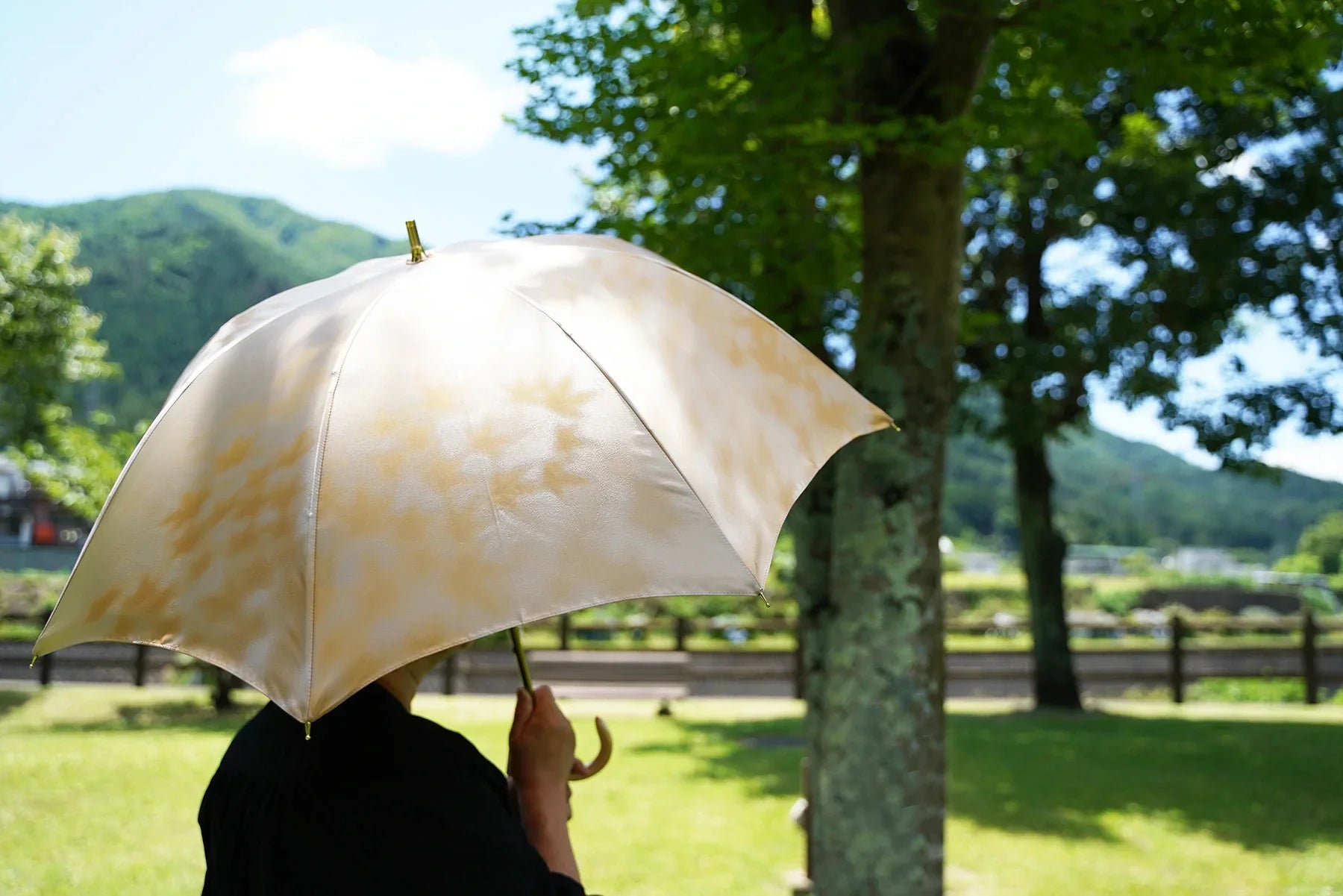 黄色のカエデ柄の晴雨兼用日傘を差す女性
